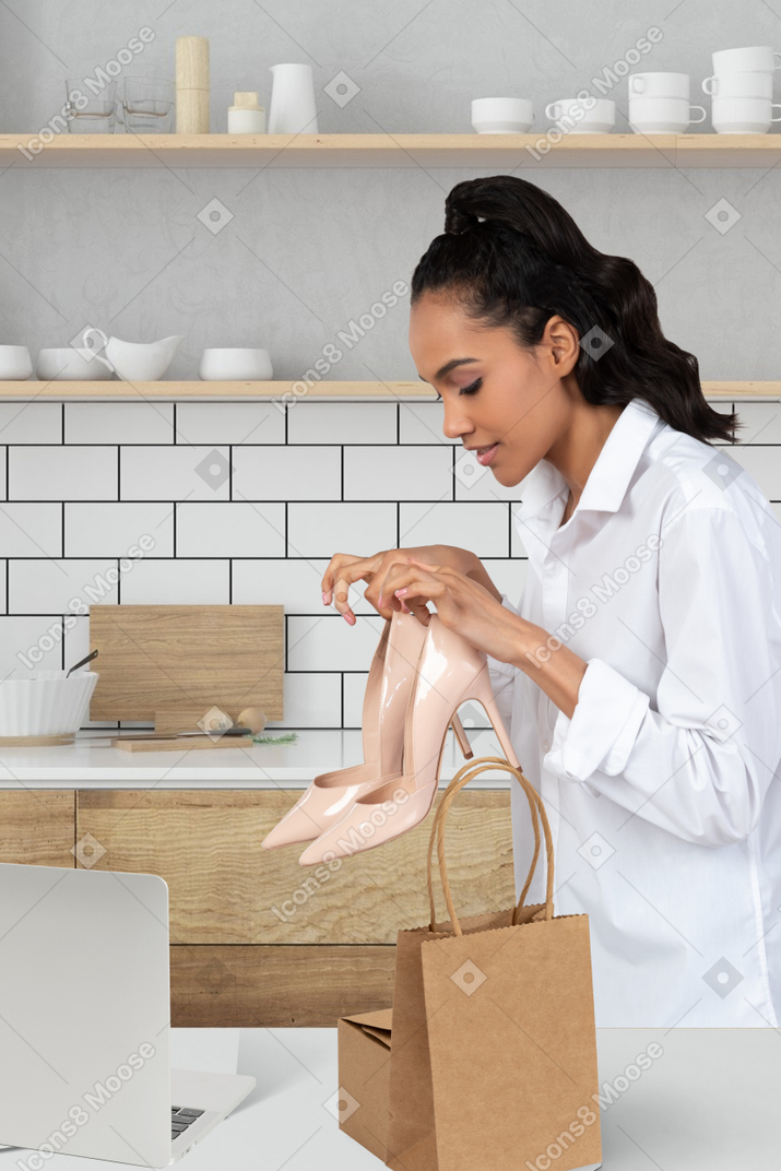 A woman holding a pair of shoes in front of table with laptop