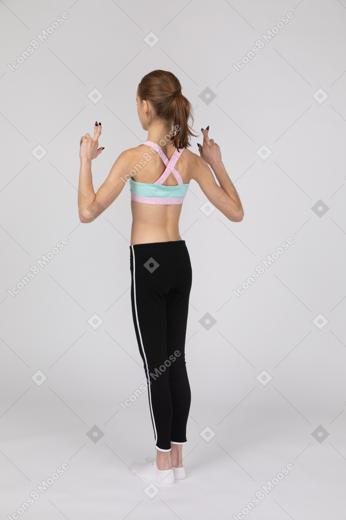 Vista de três quartos de uma adolescente em roupas esportivas cruzando os dedos