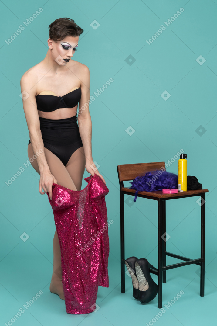 Drag queen en conjunto de ropa interior negra quitándose el vestido rosa