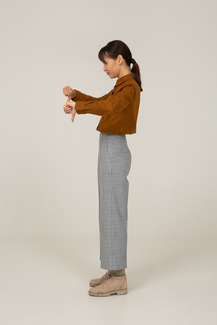 Side view of a young asian female in breeches and blouse showing thumbs down