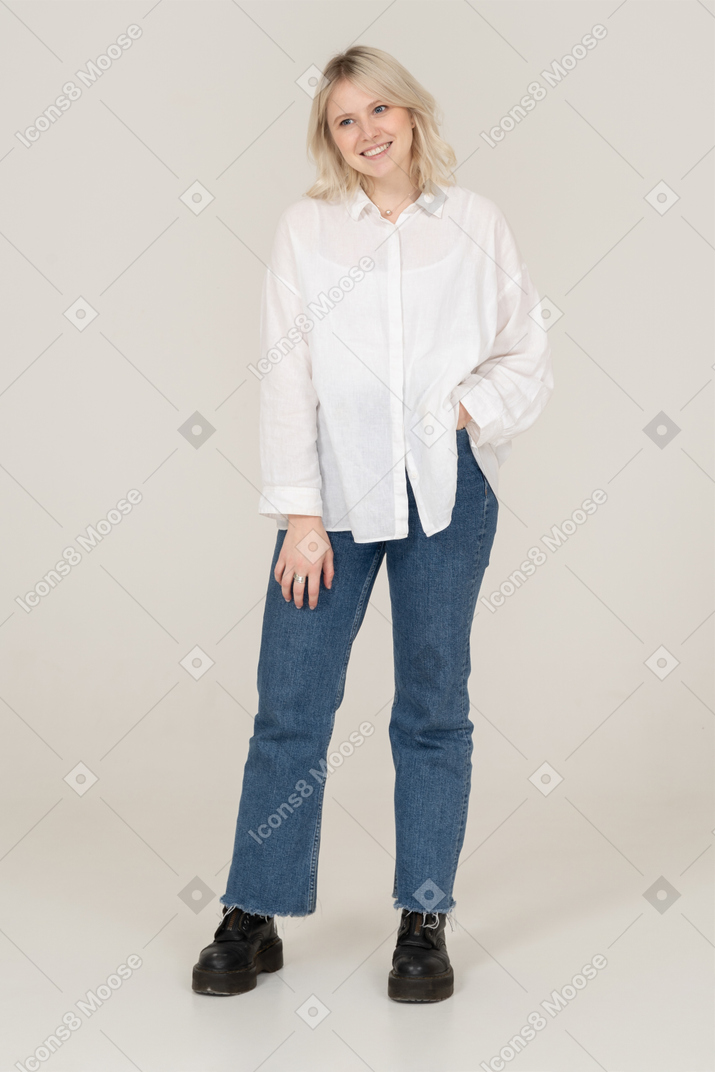 Vista frontal de uma jovem sorridente em roupas casuais, colocando as mãos no bolso e olhando para o lado
