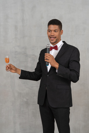 Homem com microfone e vidro de flauta propondo um brinde