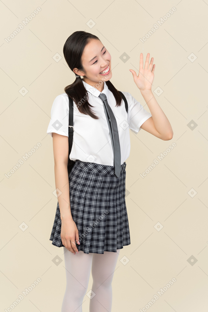 こんにちはを振って笑顔のアジアの学校の女の子