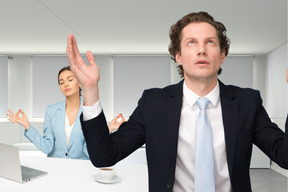 Stressed man standing in front of woman meditating at her workplace