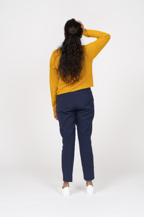 Rear view of a girl in casual clothes standing with hand on head