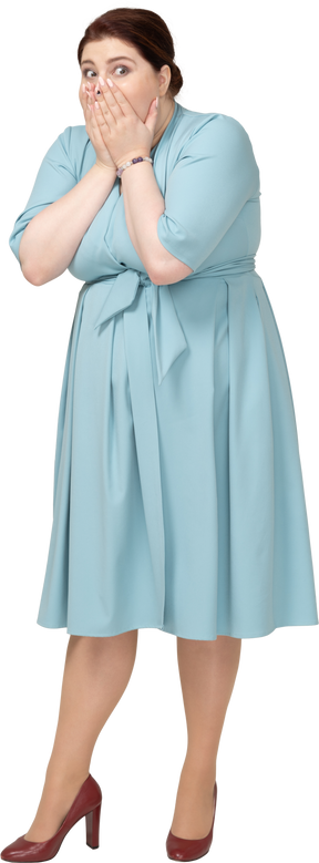 Вид спереди потрясенной женщины в синем платье, закрывающей рот руками
