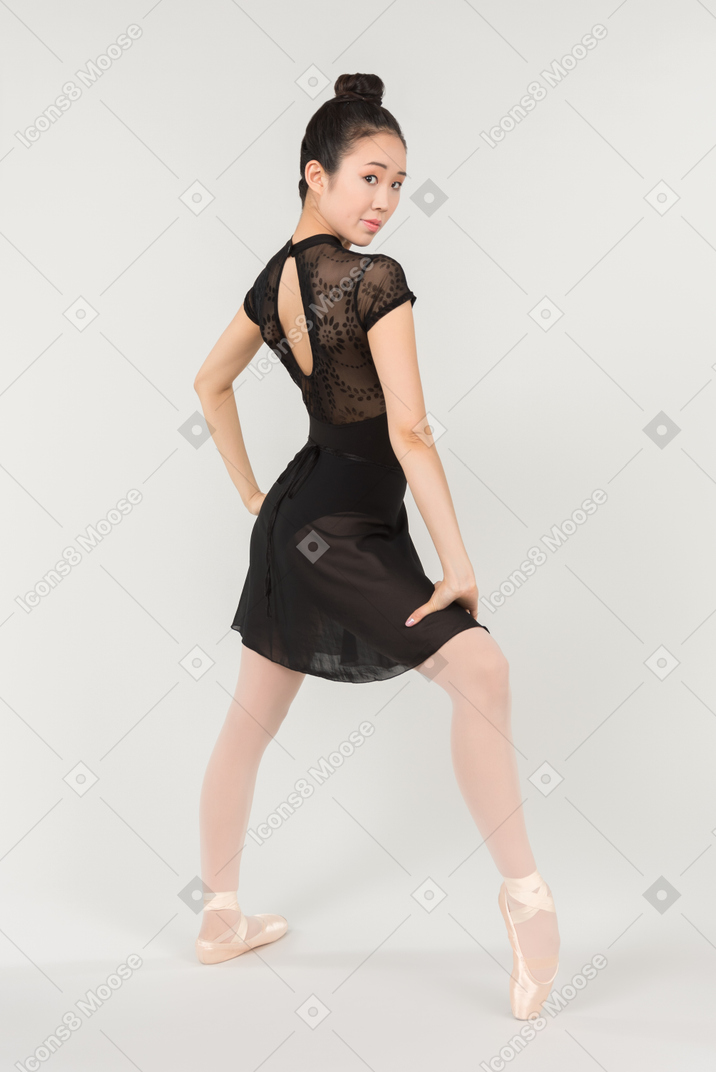 Jovem bailarina asiática pé meio lateralmente em posição para a câmera