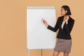 Jolie femme afro debout près du tableau blanc et expliquant certaines choses