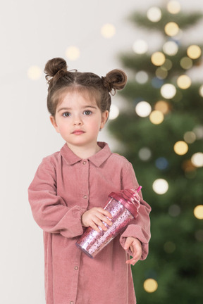 A little girl in pink shirt standing in front of a christmas tree