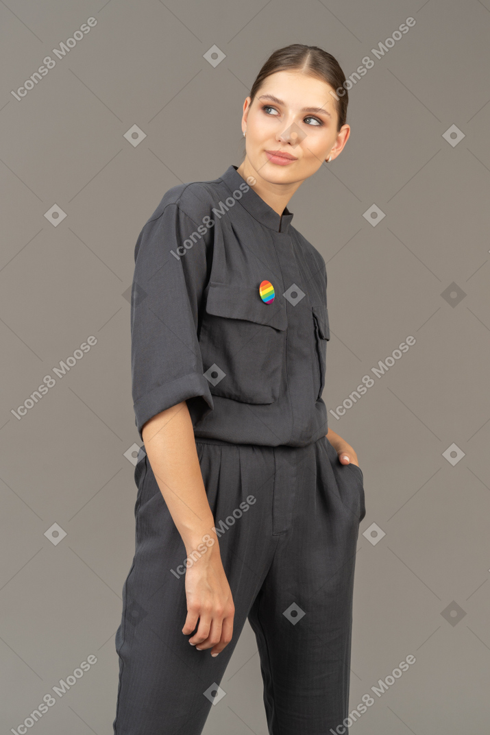 Front view of a young woman in a jumpsuit with lgbt pin putting hand in pocket