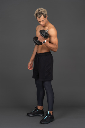 Three-quarter view of a shirtless afro man lifting the dumbbell