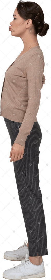 Vista laterale di una giovane donna in piedi ancora in pullover e pantaloni mettendo la mano sui fianchi e imbronciato