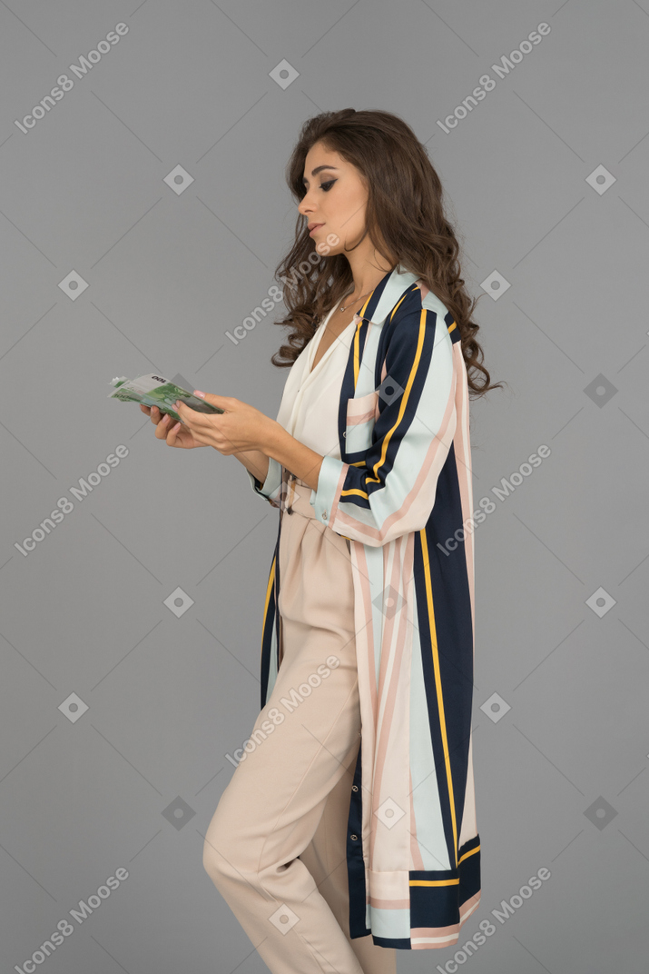 Emotionless young woman looking down at money in her hands