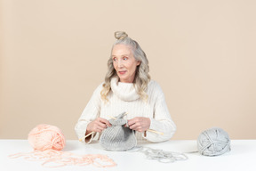 Donna invecchiata focalizzata sul lavoro a maglia e guardando da parte