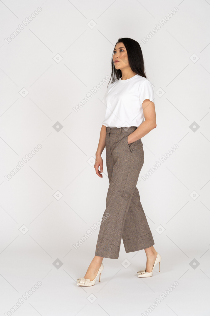 Vista di tre quarti di una giovane donna che cammina in calzoni e t-shirt che osserva da parte