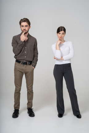 Front view of a thoughtful young couple in office clothing touching chin