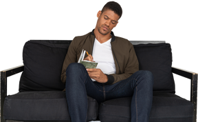 Front view of young man sitting on a sofa and making notes