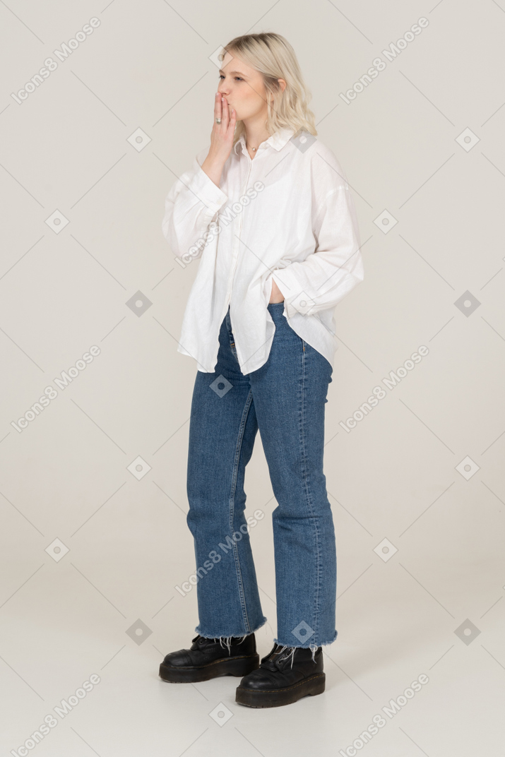 Three-quarter view of a young female in casual clothes hiding her mouth and putting hands in pocket