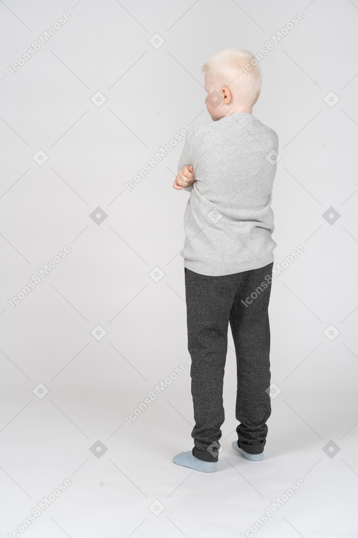 Vista traseira de três quartos do menino com as mãos cruzadas, olhando de lado