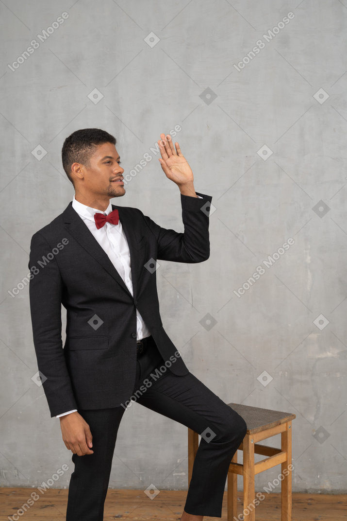 Front view of a man in black suit waving hello