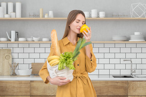 A woman holding grocery bag with food and smelling bell pepper