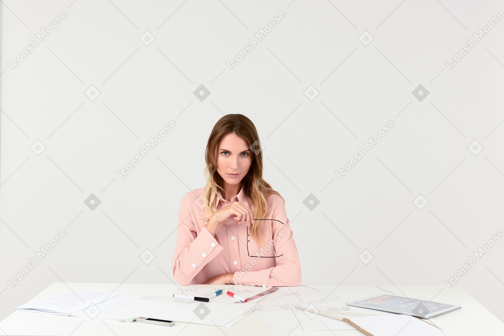 Женщина-архитектор сидит за столом и держит очки
