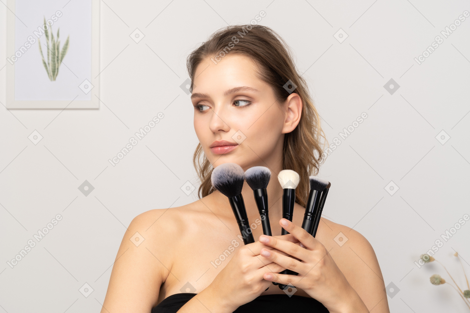 Vista frontal de una mujer joven sensual sosteniendo pinceles de maquillaje