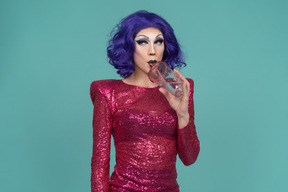 Drag queen in pink sequin dress looking sideways while having a drink