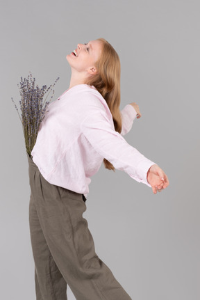 Smiling young woman standing with the flowers in her pants and arms open