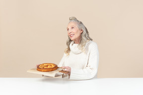 Elegante alte frau mit einem frisch gebackenen kuchen zufrieden