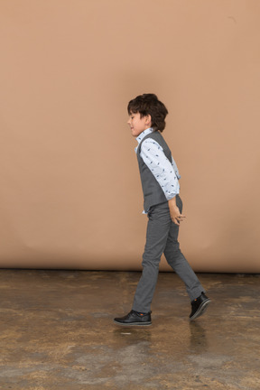 Vista lateral de un niño con traje gris caminando