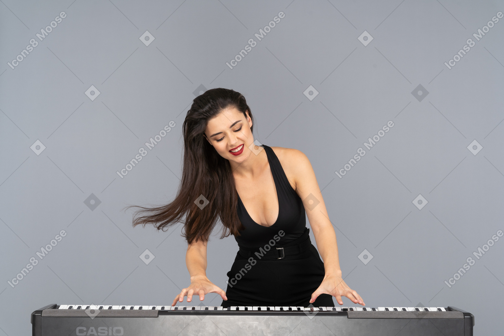 Вид спереди довольной молодой леди в черном платье, играющей на пианино, улыбаясь