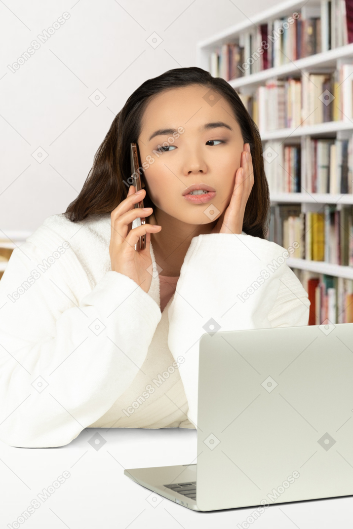 A woman sitting in front of a laptop computer talking on a cell phone