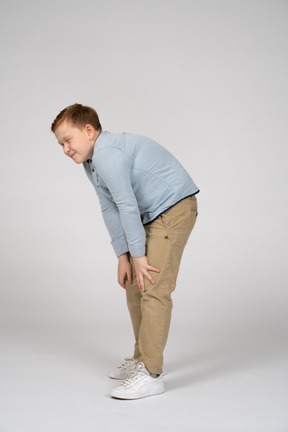 Vista lateral de un niño agachándose y tocando las rodillas lastimadas