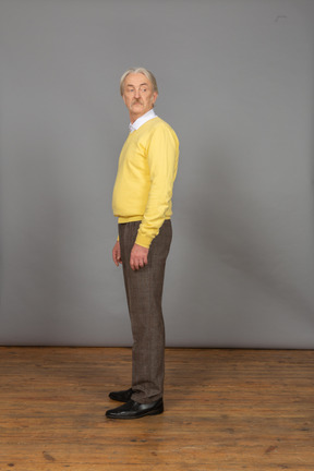 Side view of an old curious man in yellow pullover turning head and looking aside