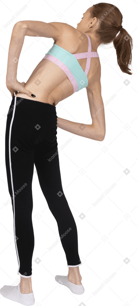 Vista posteriore di tre quarti di una ragazza adolescente in abbigliamento sportivo che mette le mani sui fianchi mentre si appoggia a destra