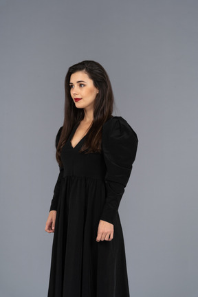 Three-quarter view of a smiling young lady in a black dress standing still