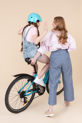 Young woman helping teen girl to ride on the bike without hands