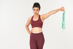 Young indian woman in sportswear looking with disgust on cloth ruler