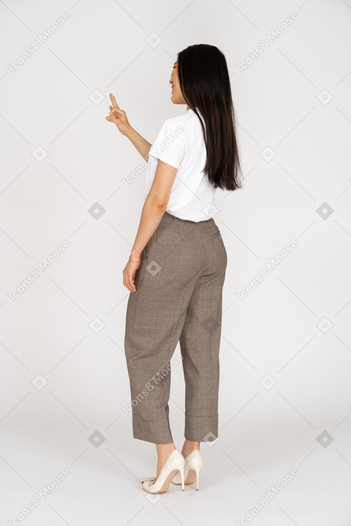 Vista posteriore di tre quarti di una giovane donna sorridente in calzoni che mostra il segno giusto