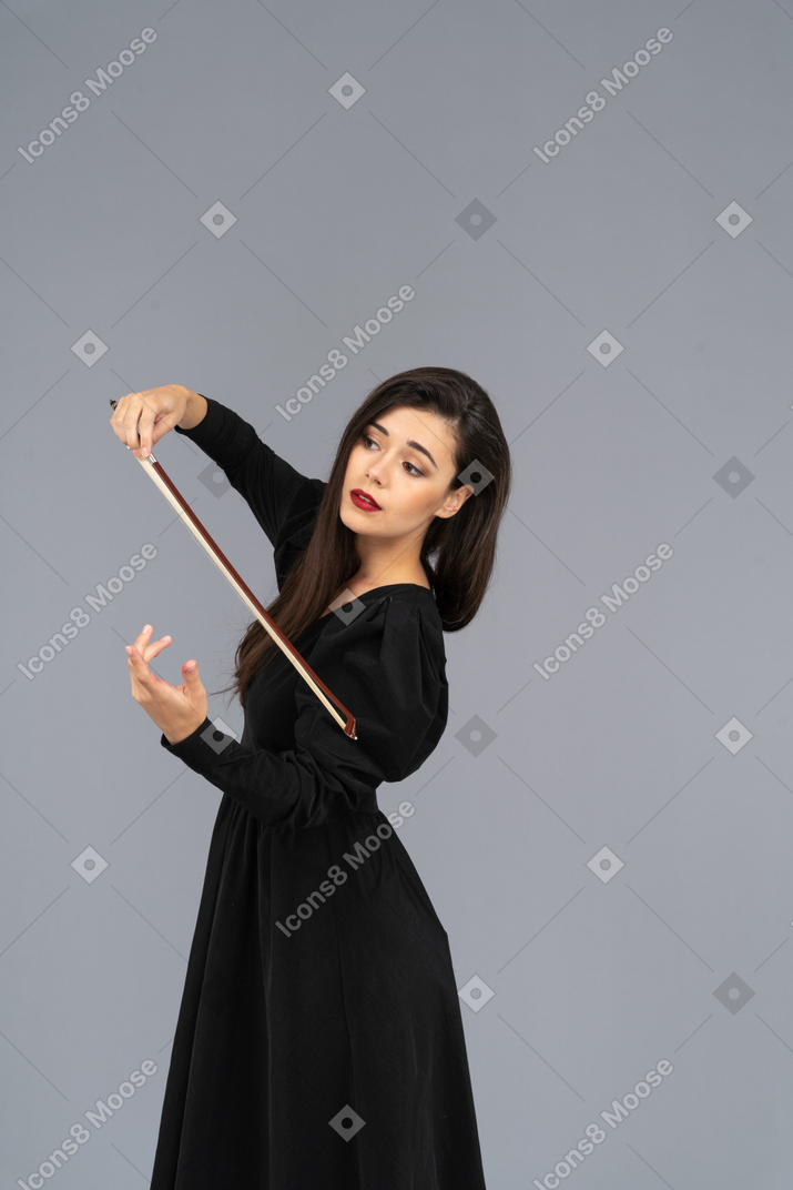 Dreiviertelansicht einer jungen dame in schwarzem kleid, die den eindruck erweckt, geige zu spielen
