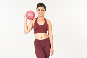 Young indian woman in sportswear holding ball on shoulder