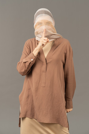Young woman covered with shawl showing shush gesture
