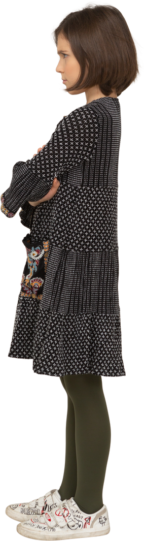 Обиженная маленькая девочка в платье, скрещивающая руки, вид сбоку