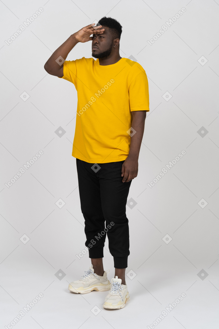 Three-quarter view of a young dark-skinned man in yellow t-shirt looking for something