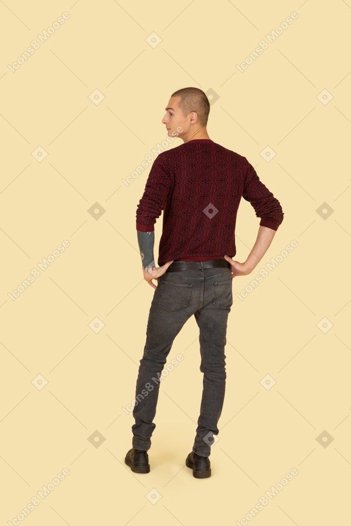 Vista traseira de um jovem de camisola colocando as mãos na cintura