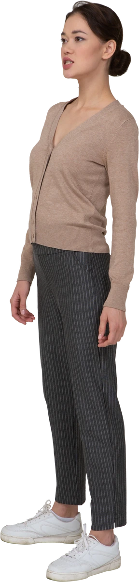 Three-quarter view of a young lady standing still in pullover and pants looking aside