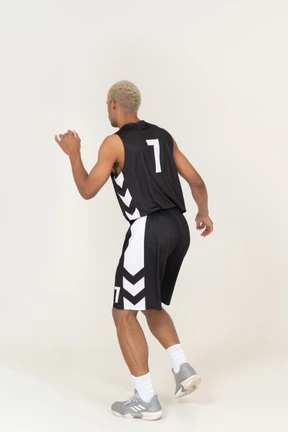 Vista posterior de tres cuartos de un confundido joven jugador de baloncesto haciendo una finta