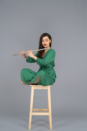 Full-length of a young lady looking at the clarinet sitting with her legs crossed on a wooden chair