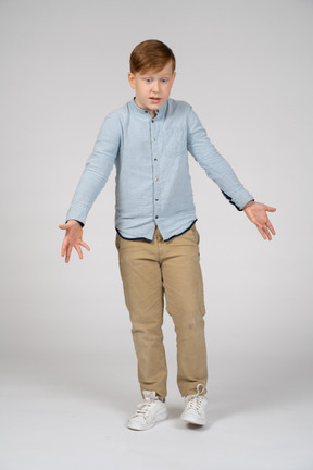 Front view of a confused boy standing with outstretched arms